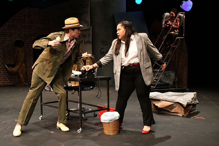 An actor portraying "Man with Ice Cream" wearing a straw brimmed hat menaces the actor playing Marisol, who is dressed for the office