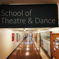 School of Theatre & Dance sign hanging above the hallway of the School. There are bulletin boards, doors, and lights stretching into the distance