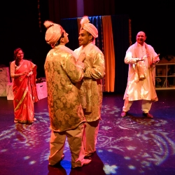 Four actors in South Asian wedding attire dance onstage in saturated lighting