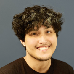 A younger man with thick dark hair and a brown t-shirt smiling at the camera