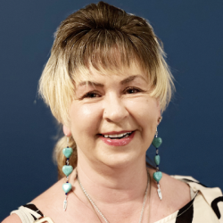 An older woman with short hair that is dark on top and bleached on the sides wearing fabulous drop earrings and smiling at the camera