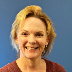 An older woman with chin-length styled blonde hair and a v-neck shirt smiling at the camera