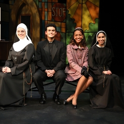 Four actors sitting together onstage and smiling. Two are dressed as nuns, one is dressed as a priest, and one is dressed in a nice mauve suitdress from the 1960s