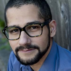 Hatem Adell, with short cropped dark hair and a widow's peak, trimmed goatee and mustache, wearing a blue button-downshirt and glasses