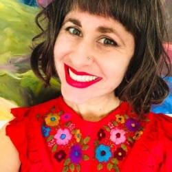 Selfie headshot of Stephanie Sherman, a woman with shoulder-length dark hair and bright red lipstick, wearing a bright red blouse with embroidered flowers across the neck and down the bodice.