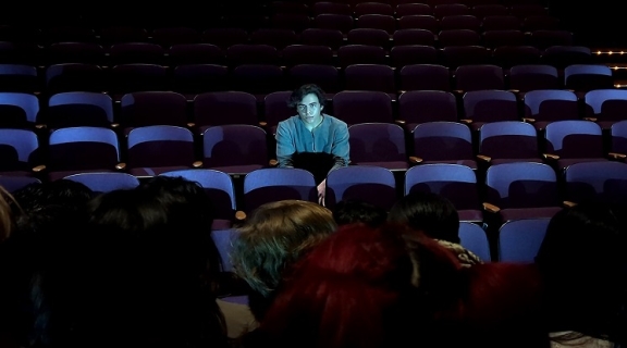 A man sitting in an empty row of theater seats